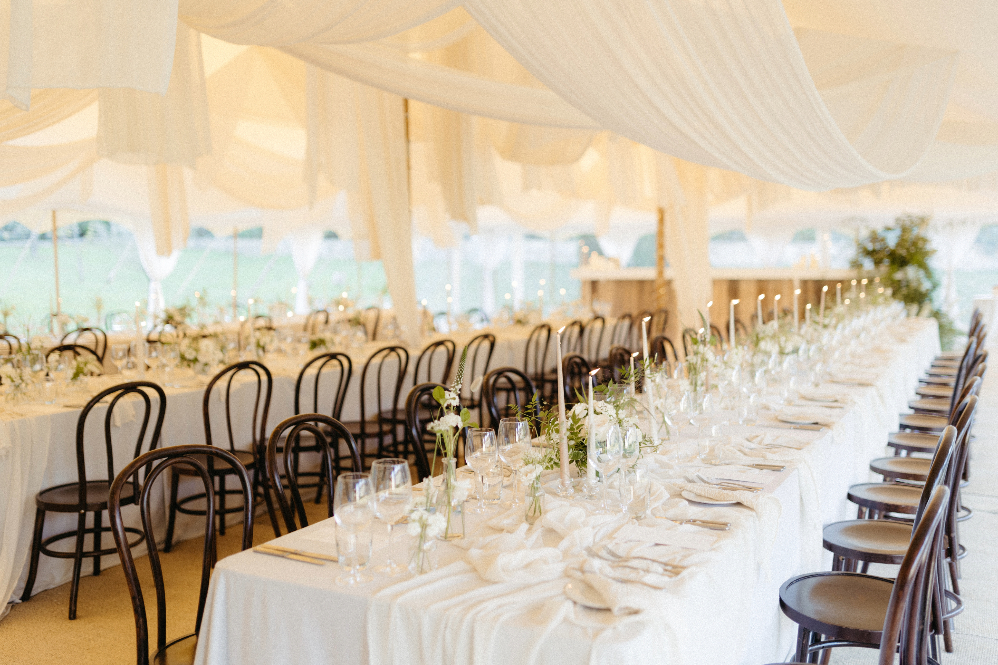 Luxury modern white wedding in a canvas marquee with beautiful draping and long tables set for dining with candles and minimalist greenery decor