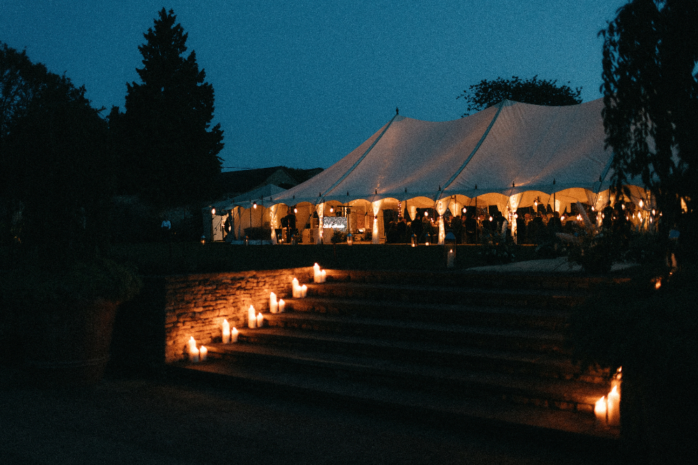 Candlelit wedding marquee for a romantic outdoor wedding reception in a private home. Candles decorate the steps up to the luxury marquee where guests are dining and dancing long into the night