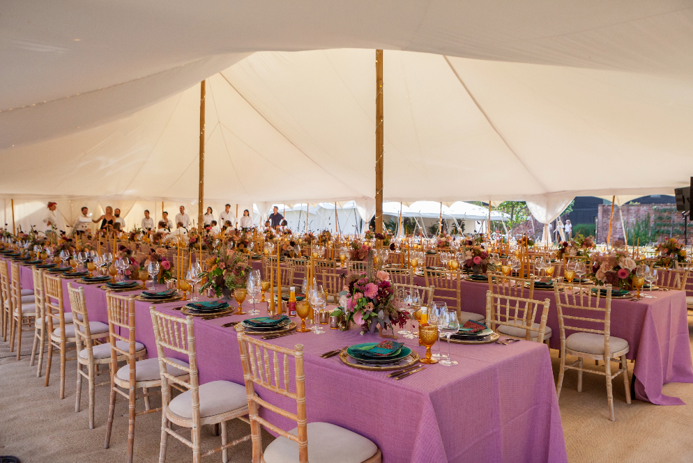 Modern luxury marquee wedding with colourful details. Pink linen and bright florals decorate the long banquet tables in a white canvas marquee with two poles